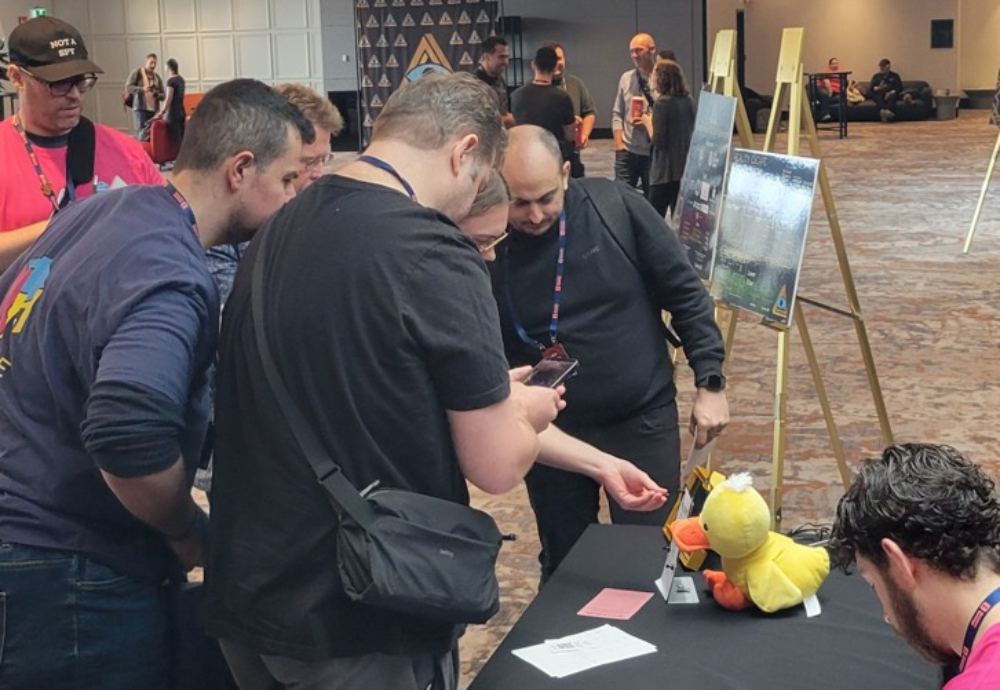 Image of RECON 26 attendees at the information desk, interacting with the event screen as part of the RECON 26 game.