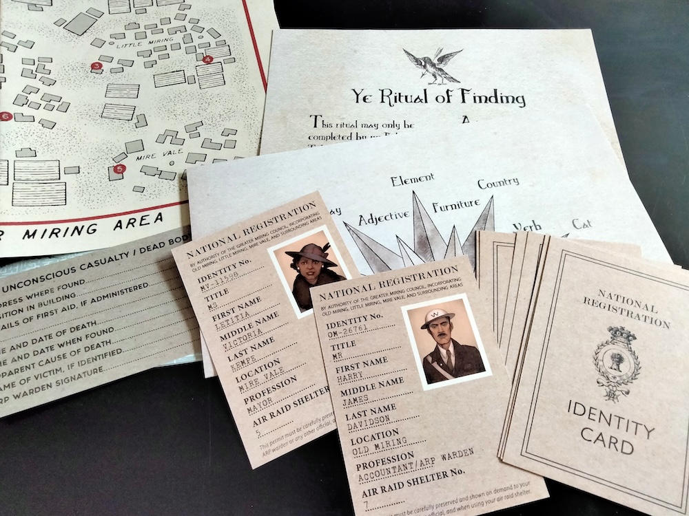 Game materials from The Witching Hour, including a set of ID cards marked "National Registration Identity Card," a hand-drawn map, and a document marked "Ye Ritual of Finding."