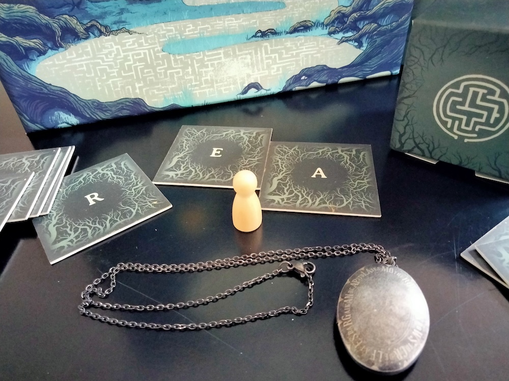 Game materials from The Witching Hour, including tiles with a tree branch design and letters on them, a game piece, and a metal locket on a chain.