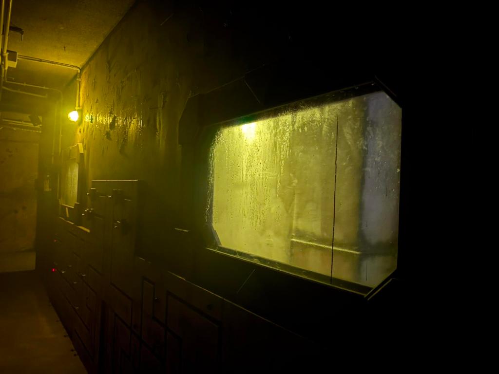 View of a dark wall with a backlit window, a single light illuminates the far side of the wall.