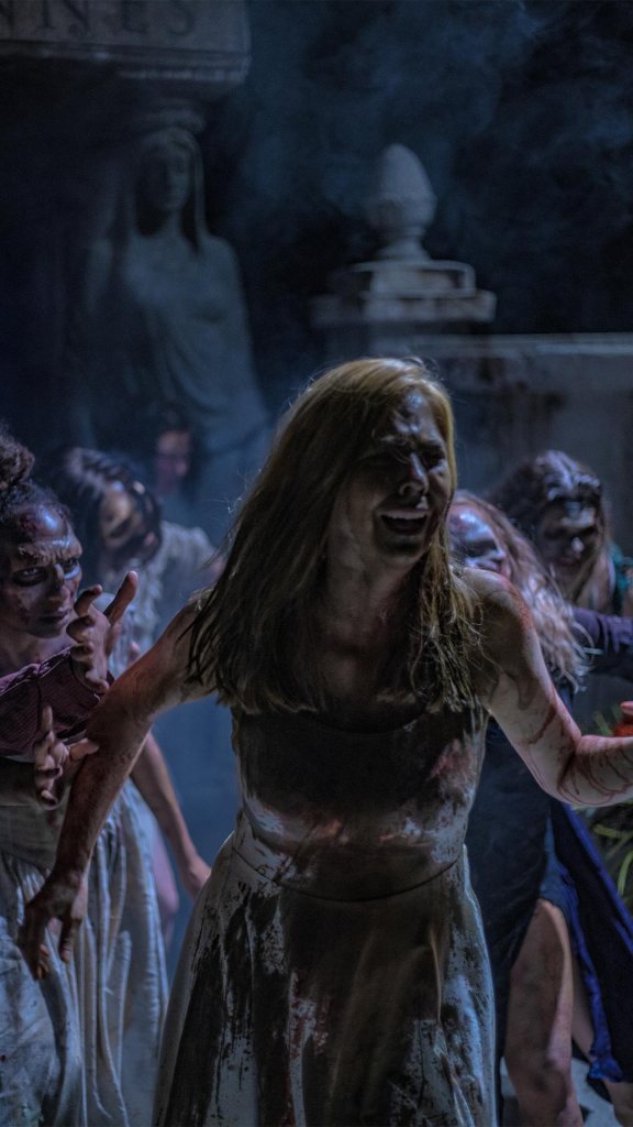 girl in white dress covered in mud and gore, panicked, running from crown of bloody zombies