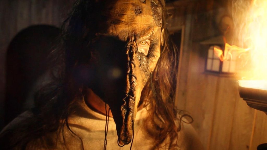 close up of man in a skin mask that is laced up the front of the face into an extended snout