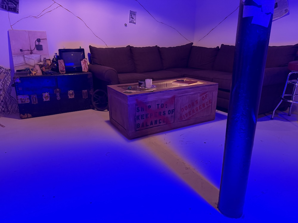 A wide open space with a shipping crate and a couch. There are some cracks in the wall beyond.